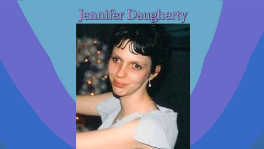 Image is a photo of Jennifer Daugherty on a background of lavender and pastel blues. Below the photo is what appears to be a platform where the photo rests. Jennifer is smiling as she is dancing at an event. Text outlined in lavender reads: Jennifer Daugherty. Always remembered.