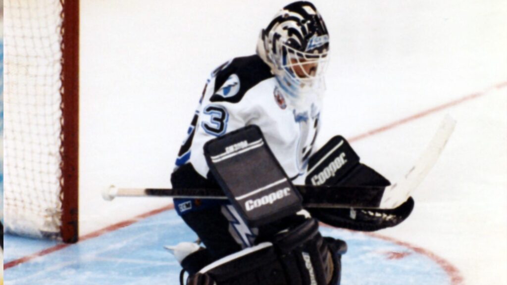 Photograph of Manon Rhéaume donning the Tampa Bay Lightning jersey, as she absorbs a shot, playing in an NHL game.