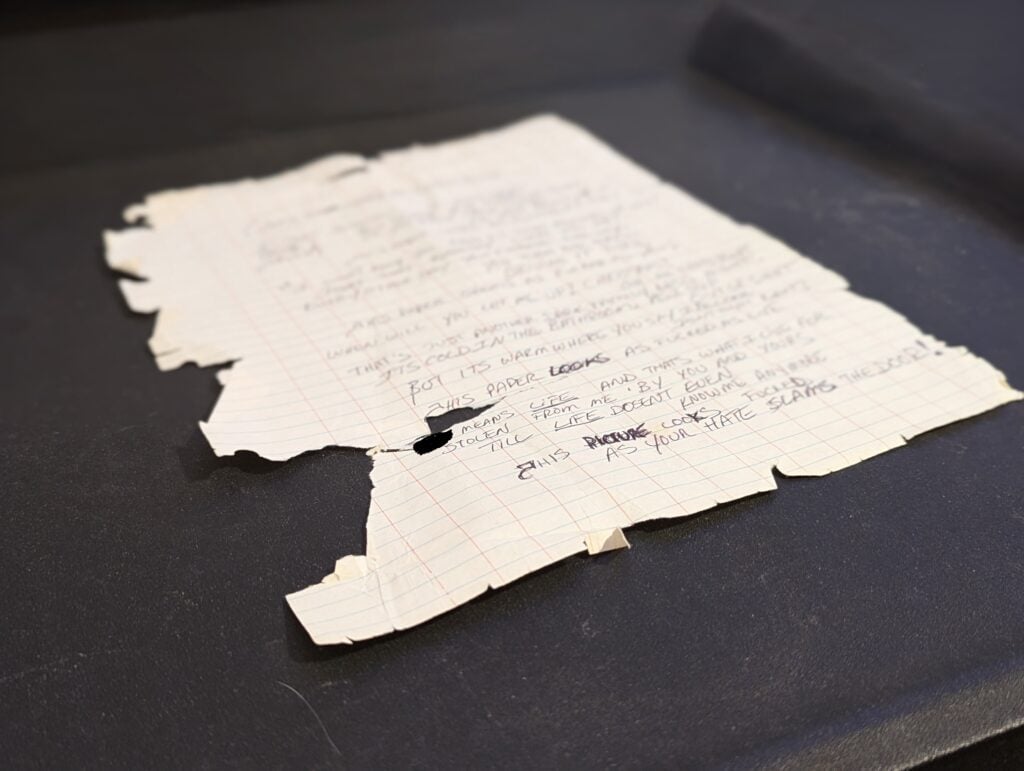 Photograph of the original draft of this poem depicting how fucked this paper actually is. A piece of looseleaf paper with handwriting on it, was chartered, shredded and riddled with holes.