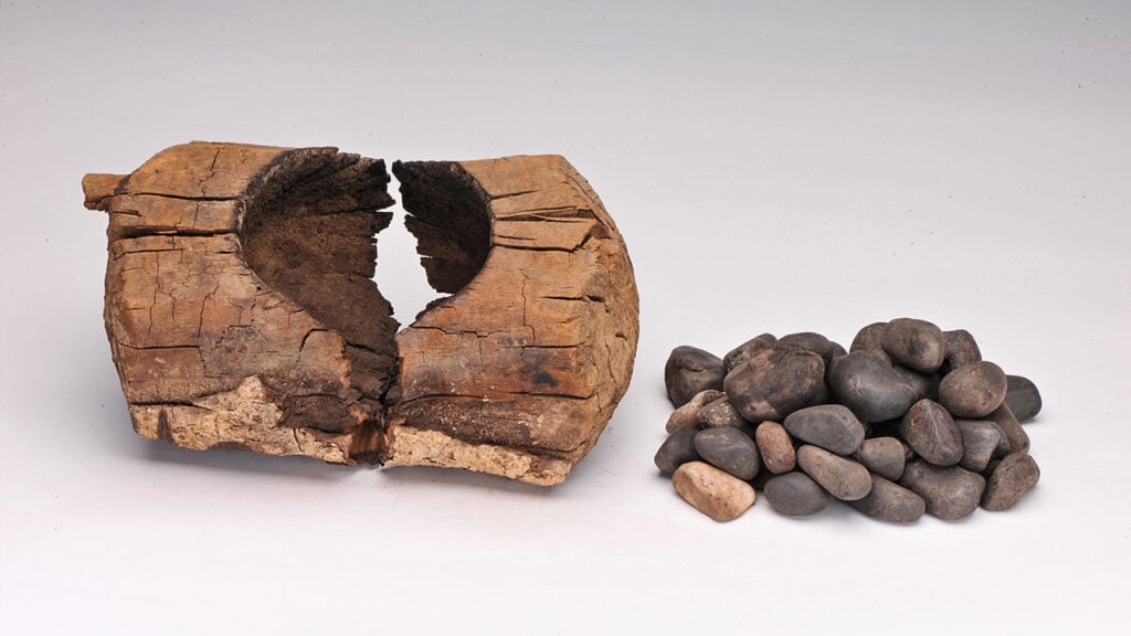 Photograph of an ancient wooden brazier found in China and pictured with a number of stones. It is believed that cannabis was placed inside with heated stones to produce smoke, that was then inhaled.